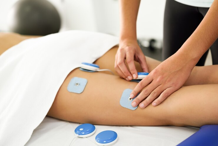 A patient receiving electronic muscle stimulation therapy on their leg in a medical setting.